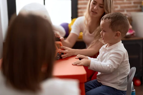 Teacher with boy and girl playing with cars toy sitting on table at kindergarten