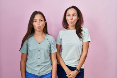 Young mother and daughter standing over pink background making fish face with lips, crazy and comical gesture. funny expression. 