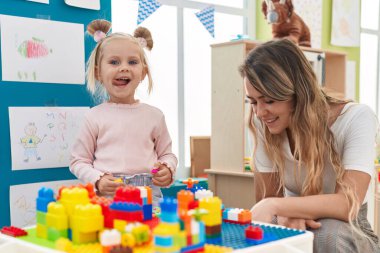 Teacher and toddler playing with construction blocks sitting on table at kindergarten