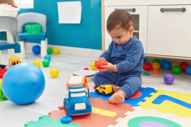 Sevimli İspanyol çocuk elinde top tutarak anaokulunda yerde oturuyor.