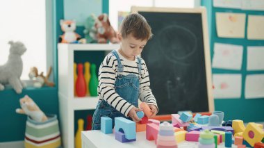 Adorable caucasian boy playing with construction blocks at kindergarten