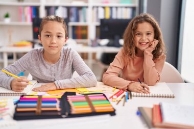 Two kids students sitting on table drawing on notebook paper at classroom