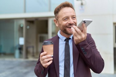 Orta yaşlı bir iş adamı akıllı telefondan konuşuyor sokakta kahve içiyor.