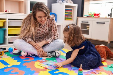 Teacher and toddler playing with maths puzzle game sitting on floor at kindergarten