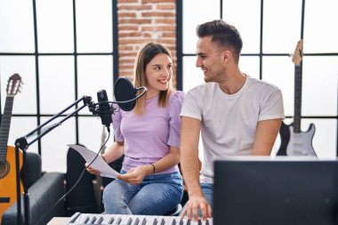 Erkek ve kadın müzisyenler müzik stüdyosunda piyano çalarak şarkı söylüyorlar.