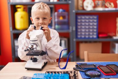 Adorable toddler student using microscope standing at classroom
