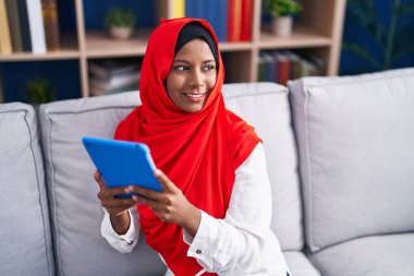 Young beautiful woman using touchpad sitting on sofa at home