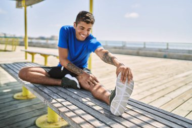 Genç İspanyol adam dışarıda bacak kaslarını esnetiyor.