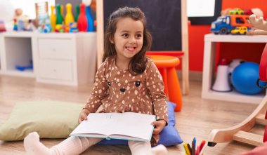 Anaokulunda yerde oturmuş kitap okuyan sevimli İspanyol kız.