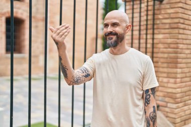 Young bald man smiling confident doing coming gesture with hand at street