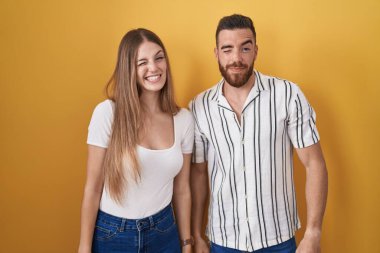 Young couple standing over yellow background winking looking at the camera with sexy expression, cheerful and happy face. 
