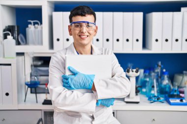 Young non binary man scientist smiling confident hugging binder at laboratory