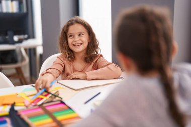Two kids students sitting on table drawing on notebook paper at classroom