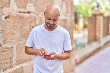 Sokakta akıllı telefon kullanarak kendine güvenen genç kel adam.