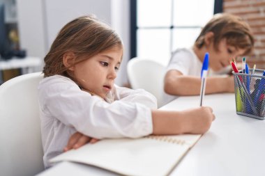 Erkek ve kız kardeş öğrencileri sınıfta ders çalışırken deftere yazıyorlar.