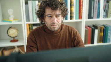 Young hispanic man student using computer studying at library university