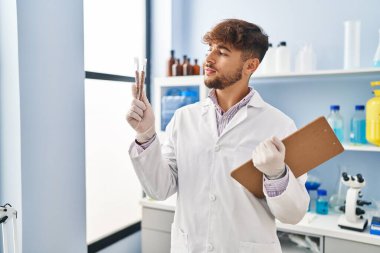 Young arab man scientist holding test tube and clipboard at laboratory