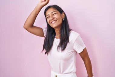 Young hispanic woman standing over pink background dancing happy and cheerful, smiling moving casual and confident listening to music 