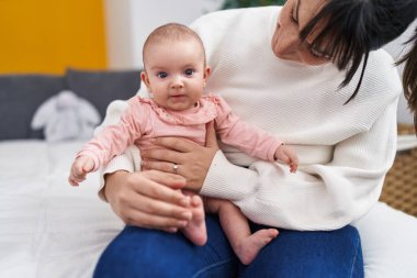 Mother and daughter smiling confident sitting on bed at bedroom