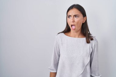 Young hispanic woman standing over white background angry and mad screaming frustrated and furious, shouting with anger. rage and aggressive concept. 