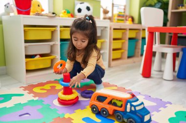 Adorable hispanic girl playing with hoops toys sitting on floor at kindergarten