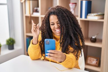 Plus size hispanic woman using smartphone sitting on the table smiling happy pointing with hand and finger to the side 