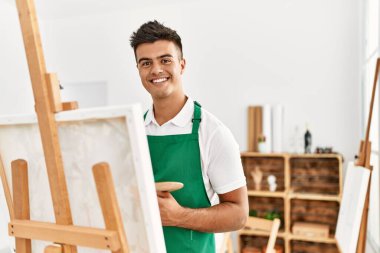 Genç İspanyol adam resim stüdyosunda kendine güvenen gülümsüyor.
