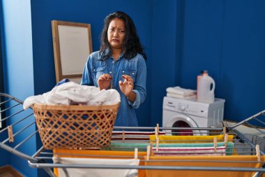 Young asian woman hanging clothes at clothesline disgusted expression, displeased and fearful doing disgust face because aversion reaction. with hands raised 