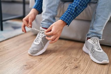 Young redhead man tying shoe sitting on sofa at home