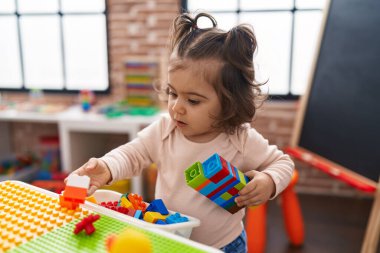 Adorable hispanic girl playing with construction blocks standing at kindergarten