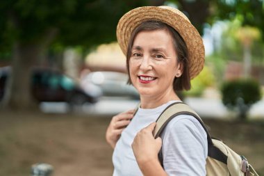 Orta yaşlı bir turist parkta sırt çantası takıp gülümsüyor.