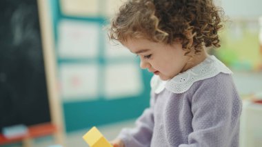 Adorable hispanic girl playing with construction blocks standing at kindergarten