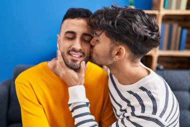 İki erkek birbirine sarılıyor ve evdeki koltukta öpüşüyorlar.