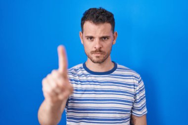 Mavi arka planda dikilen genç İspanyol adam parmağını kaldırmış ve kızgın bir ifadeyle işaret ediyor, hiçbir hareket göstermiyor. 