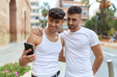 Two hispanic men couple smiling confident using smartphone at street