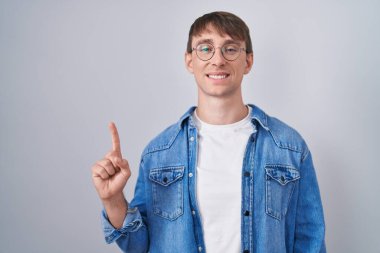 Caucasian blond man standing wearing glasses showing and pointing up with finger number one while smiling confident and happy. 