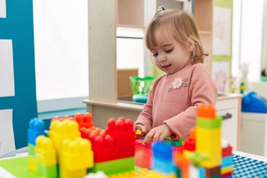 Adorable blonde girl playing with construction blocks standing at kindergarten