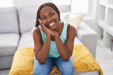 Afro-amerikalı bir kadın evdeki koltukta kendinden emin bir şekilde oturuyor.