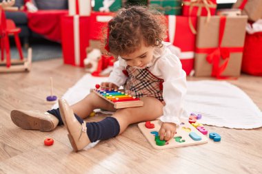 Adorable hispanic girl playing with maths game sitting on floor by christmas tree at home