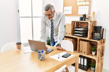 Orta yaşlı, kır saçlı, çağrı merkezi ajanı ofiste çalışırken kendinden emin gülümsüyor.