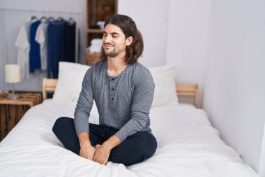 Young hispanic man sitting on bed meditating at bedroom