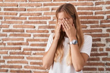 Young caucasian woman standing over bricks wall rubbing eyes for fatigue and headache, sleepy and tired expression. vision problem 