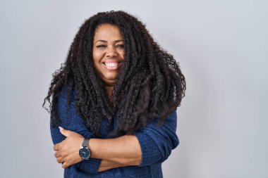 Plus size hispanic woman standing over white background happy face smiling with crossed arms looking at the camera. positive person. 