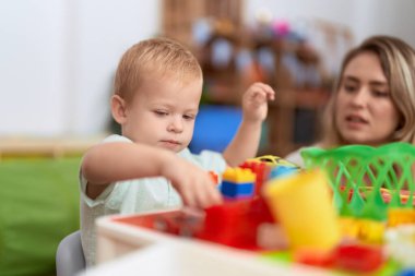 Teacher and toddler playing with construction blocks sitting on table at kindergarten