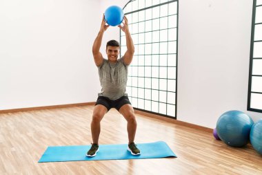 Genç İspanyol gülen adam spor merkezinde formda top kullanarak kendine güvenen bir antrenman yapıyor.