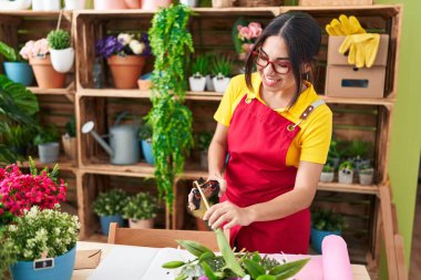 Young beautiful arab woman florist cutting plant at flower shop