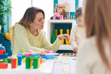 Teacher and toddler playing with maths puzzle game sitting on table at kindergarten