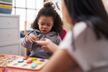 Teacher and toddler playing with maths puzzle game sitting on table at kindergarten