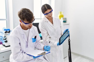 Man and woman partners wearing scientist uniform using touchpad with embryo image at laboratory