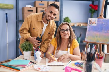 Man and woman artists drawing on notebook holding smartphone at art studio